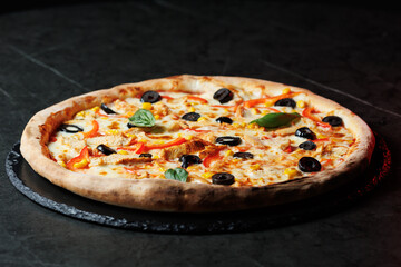 Tasty pizza with melted cheese and assorted toppings on a dark background. Perfect for menu, delivery or food promo.