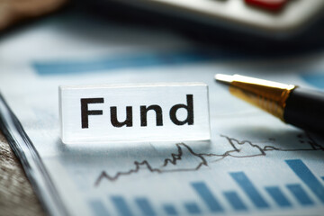 Obraz premium A clear block with 'Fund' text placed on a paper with financial charts, next to a pen.