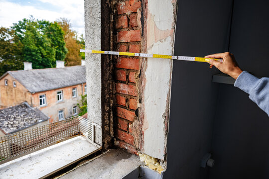 Professional measures window frame on construction site, Laborer records dimensions of brick arch for renovation work