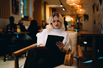 Stylish woman in white t-shirt working on tablet with stylus at café table, representing flexible digital workflow, online communication, and modern professional creativity in public space