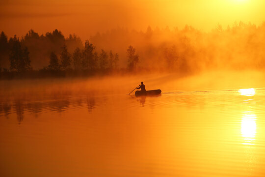 On a foggy morning at dawn, a boat with a fisherman sails in silence