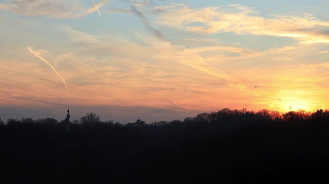 An airplane approaches DCA for landing, silhouetted against a colorful sunset. The minaret of the Washington Islamic Center is visible in the distance above the tree line.