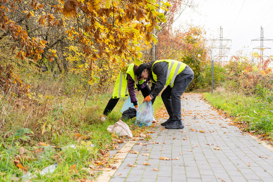 Picking fall litter. Volunteers clean up trash in an autumn park. Man and woman collect trash in bags outdoors. People Collecting Garbage in a Park