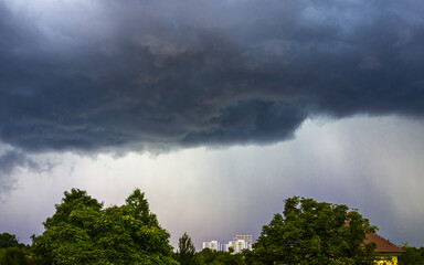 Dark thunderclouds over green trees in the city