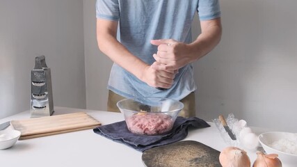Man seasoning raw ground meat with pepper from a grinder and mixing minced meat in glass bowl, while preparing homemade meatballs. Cooking, food preparation and culinary process