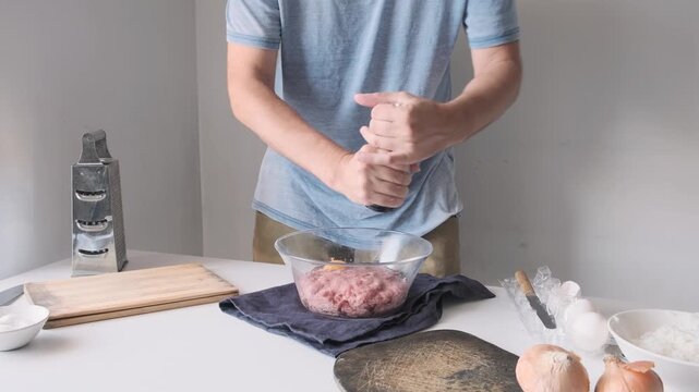 Man seasoning raw ground meat with pepper from a grinder and mixing minced meat in glass bowl, while preparing homemade meatballs. Cooking, food preparation and culinary process