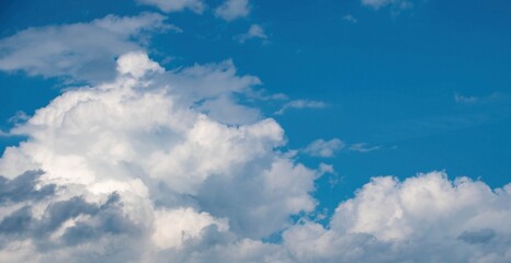 Fluffy white clouds drift across a clear blue sky on a sunny day, creating a peaceful and serene atmosphere. The scene invites relaxation and enjoyment of nature's beauty.