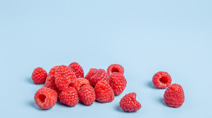 Pile of ripe red raspberries scattered on a solid light blue background with copy space