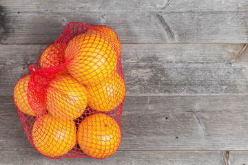 Bright yellow citrus fruit in a red mesh bag resting on rustic wooden boards.  © Gennadi