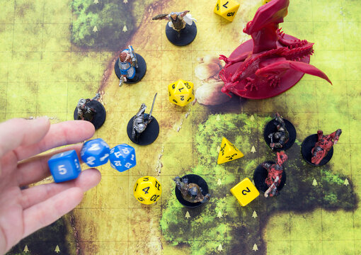 Playing Dungeons and Dragons, a role-playing game, dnd. A map with dices and characters on it, a hand throwing dices, red dragon