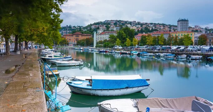 Rijeka, Croatia - August 21, 2025: Timelapse, slide transition. Quiet waterfront with small boats moored along a calm canal, reflecting colorful buildings, cloudy sky.