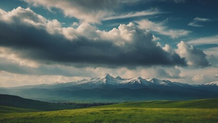Panoramic spring or summer mountain landscape green rolling hills flowering field foreground majestic snow-capped mountain peaks dramatic blue sky clouds