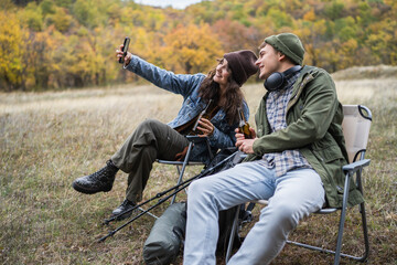 Happy young couple enjoying autumn nature taking selfie with beer