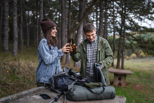 Happy couple camping, toasting beer bottles in forest