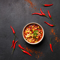 Traditional mexican dish chili con carne in ceramic bowl on black concrete background with chili peppers. Overhead view, flat lay, copy space. Minimal abstract composition