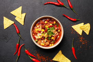 Traditional mexican dish chili con carne in ceramic bowl on black concrete background with chili peppers and nachos. Overhead view, flat lay