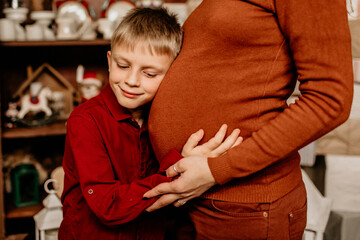 Sweet little boy hugging and listening to his pregnant mother's belly, anticipating the arrival of...