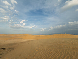  Panoramic view of desert landscape with golden sand dunes and spectacular cloudy blue sky.