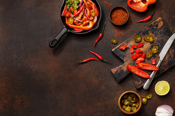 Traditional mexican dish fajitas in cast iron pan with ingredients for cooking on dark concrete background. Flat lay, frame composition with copy space. Overhead view