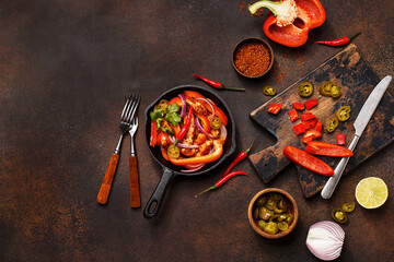 Traditional mexican dish fajitas in cast iron pan with ingredients for cooking on dark concrete background. Flat lay, overhead view, copy space