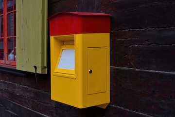 Bright yellow and red mailbox mounted on a wooden wall near a colorful window. Urban detail and communication concept.
