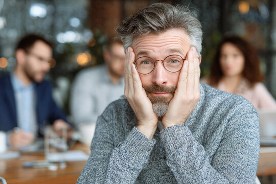 Frustrated man sitting at a table and holding his face with both hands during a conversation