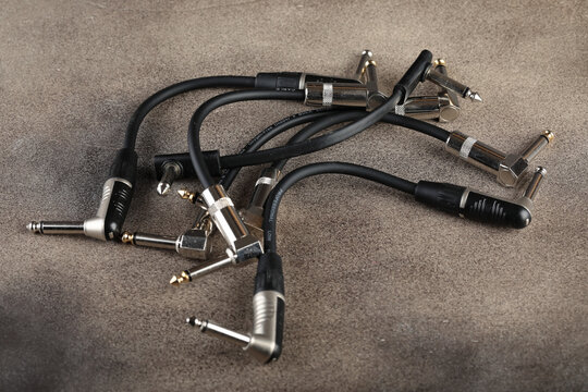 Guitar patches for connecting various pedal sound effects for electric guitars on a brown cement background. - Powered by Adobe