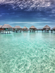 Overwater bungalows on turquoise lagoon water under a dramatic blue sky in a tropical paradise.