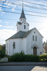 Fototapeta premium Skare Church, Haugesund, Norway, quaint white church with a pointed steeple stands on a street, surrounded by greenery and a white picket fence