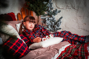 Happy little girl child in pajamas lies in bed in bedroom. Christmas. New Year. St. Nicholas Day. Time of holidays and miracles.	