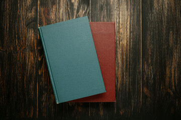 Two blank books, teal and burgundy, stacked on a dark, rich wooden back