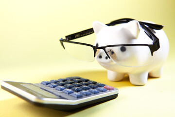Piggy bank with glasses, calculator and spectacles on yellow background