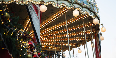 Christmas illuminated vintage carousel with lights garlands at festive holiday event. Xmas enjoy in celebratory nostalgic setting. Close up.