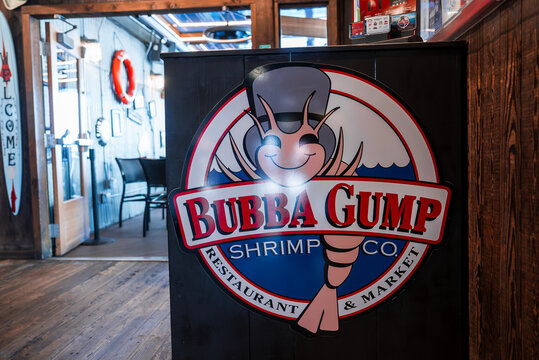 Close up of Bubba Gump Shrimp Co. logo on host stand in Monterey, California, with wooden floors, metal chairs, life preserver, bright lighting, shallow depth of field.