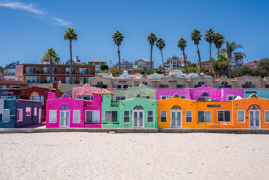 Turquoise, magenta, lime, and tangerine stucco cottages line the beach at Capitola Venetian Court in Capitola, California, midday light with crisp colors and palm trees.
