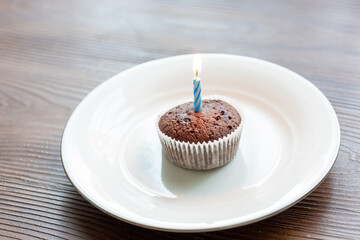 Close-Up of Chocolate Brownie Birthday Cake with a Burning Candle on a White Plate
