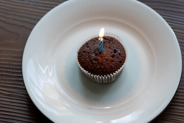 Close-Up of Chocolate Brownie Birthday Cake with a Burning Candle on a White Plate
