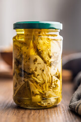 Pickled artichoke in jar on wooden table.