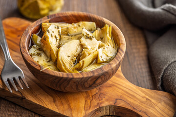 Pickled artichoke in bowl on wooden table.