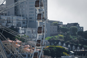 Fototapeta premium Close view of a Ferris wheel with enclosed gondolas in San Francisco, California, rising beside layered apartments and steep streets in soft coastal daylight.