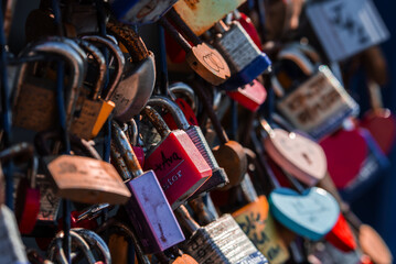 Close up view of heart shaped padlocks with initials on a railing in San Francisco, California. Sunlit shallow depth of field highlights reds, pinks, and blues.