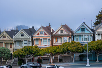 Victorian Painted Ladies line the street at Alamo Square, San Francisco. Pastel facades and trim show in soft overcast light as high rises appear through mist.