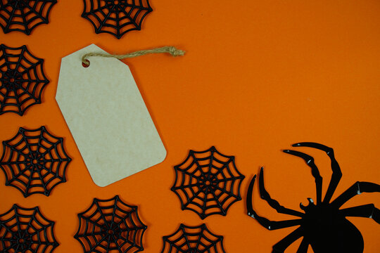 Spooky orange background featuring a black gift tag, spider webs, and a creepy spider for Halloween-themed labels, party invites, or seasonal promotions.