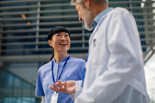 Mature medical professionals conversing outside hospital - Powered by Adobe