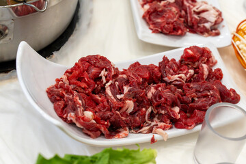 A close-up of freshly thinly sliced raw beef on a white plate, prepared for a hot pot meal. The vibrant red meat highlights freshness, protein, and Asian cuisine ingredients