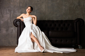 Fototapeta premium Elegant bride in minimalist wedding gown poses on luxurious couch in natural light studio setting