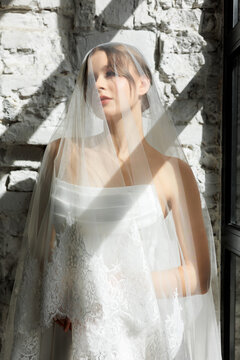 Elegant bride in a minimalist white dress poses gracefully in natural light studio setting for wedding inspiration