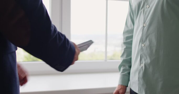 Bribe money cash exchange symbolizes corruption. A discreet payoff between men by a window, as a cash bundle moves hand to hand, implying kickback, extortion. Clear concept illicit cash bribe.