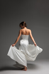 Naklejka premium Elegant bride in minimalist white dress twirls in modern studio with soft natural light
