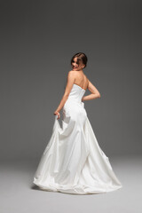 Fototapeta premium Elegant bride showcasing a minimalist white wedding gown in a modern studio setting with soft natural light